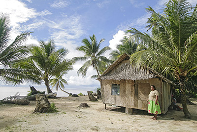 Photo by Yvette Cardozo. Local woman stands by her palm thatch house in Walung, an isolated village in Kosrae, Federated States of Micronesia (FSM)